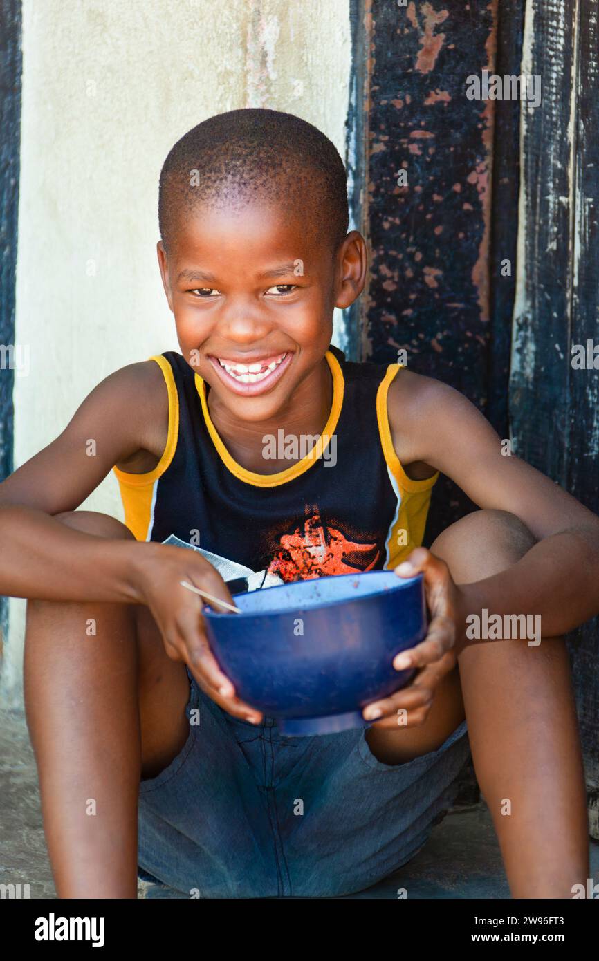 hungry child africa in a village, he is eating from a bowl in front of the house daytime Stock Photo