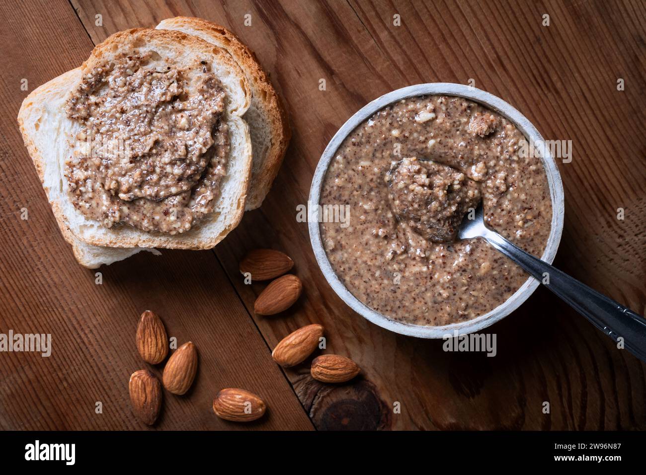 Almond butter in a bowl with almonds on a wooden background. Stock Photo