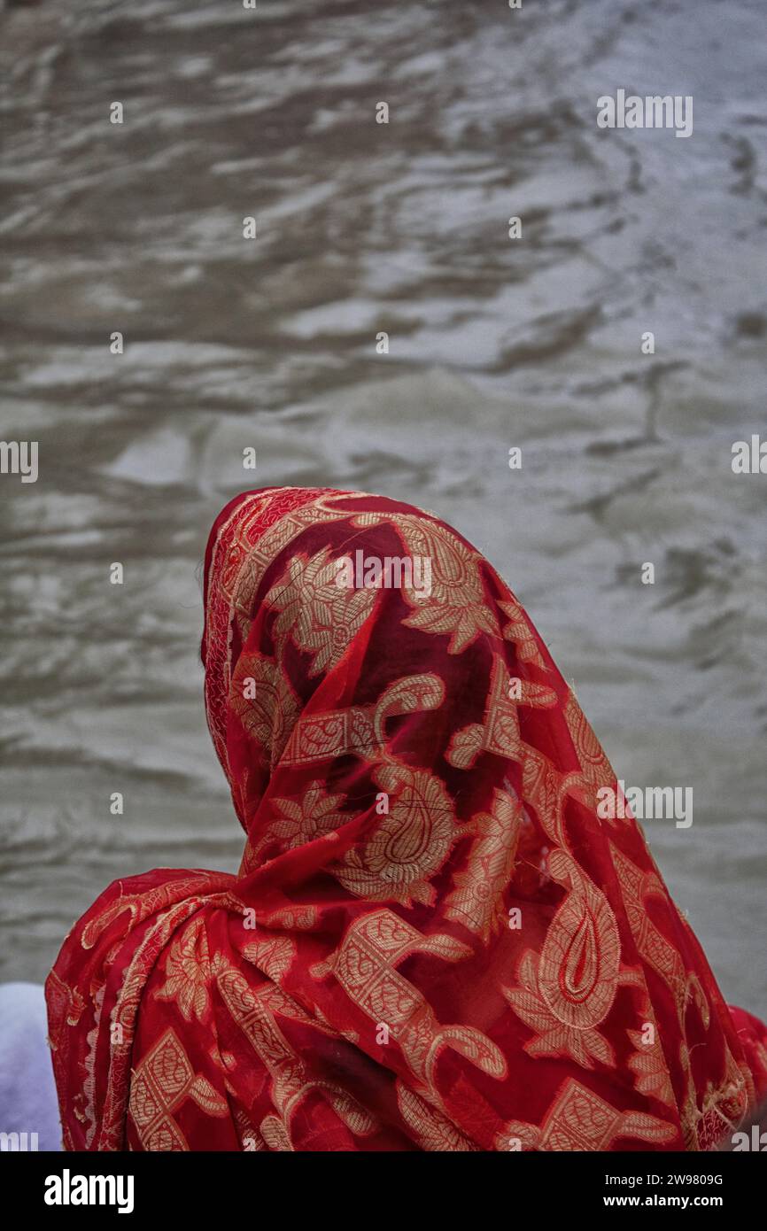 A woman in a red headscarf looking at the water. Stock Photo
