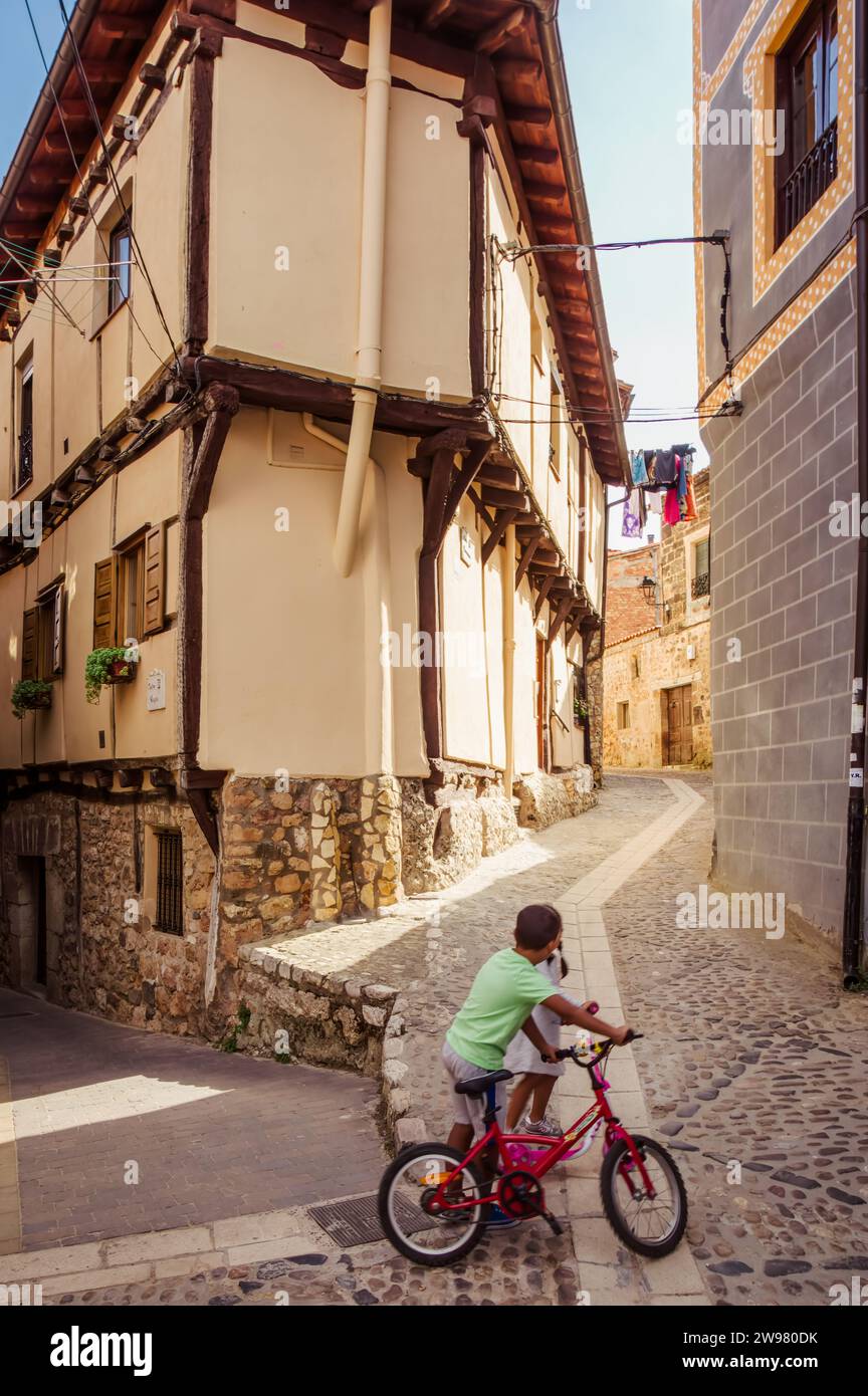 Children playing with a red bicycle through Poza del Sal (Castile and León, Spain) Stock Photo