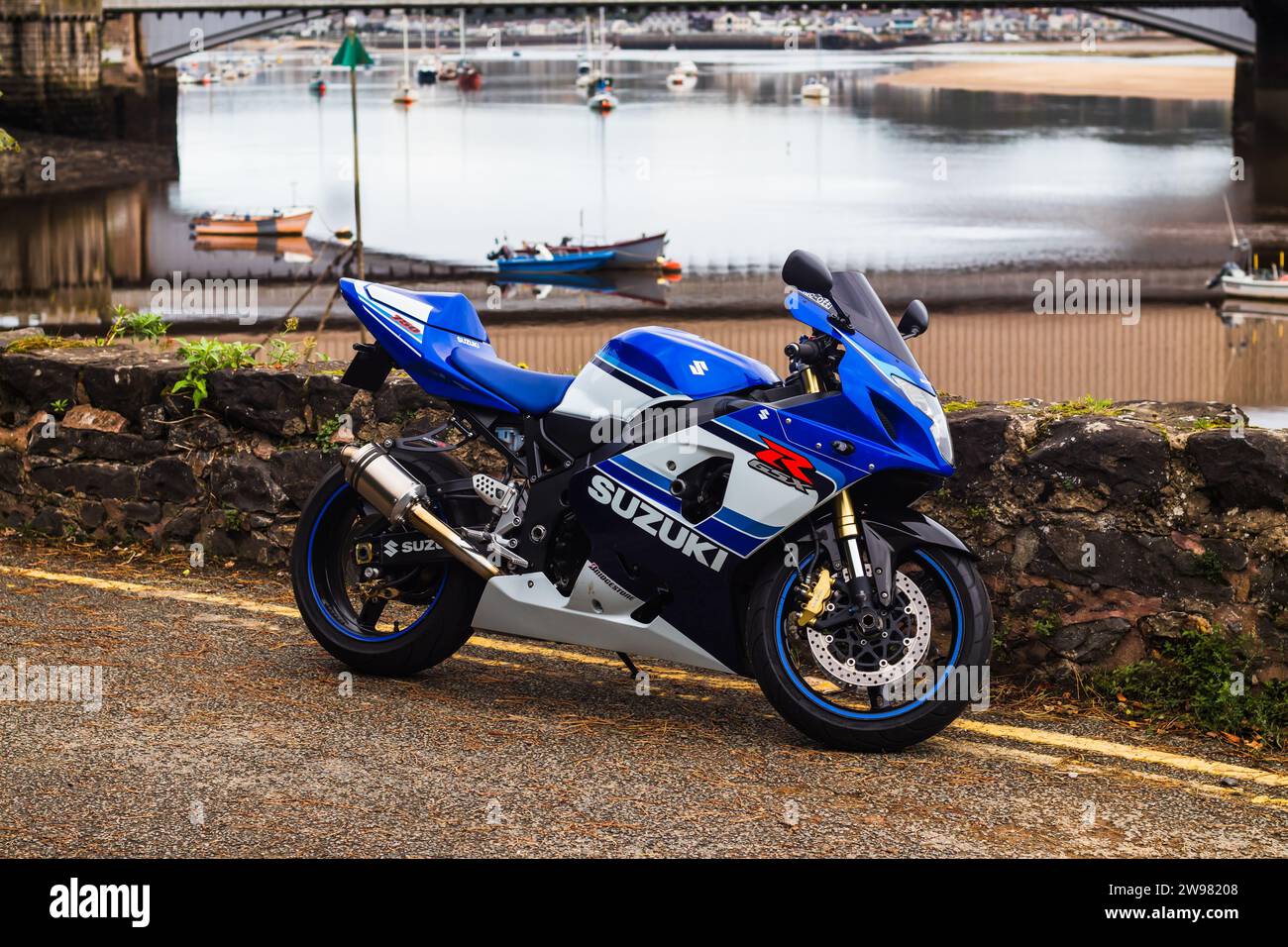 A close-up of a Suzuki motorcycle parked against a backdrop of mountains in Conwy, Wales Stock Photo