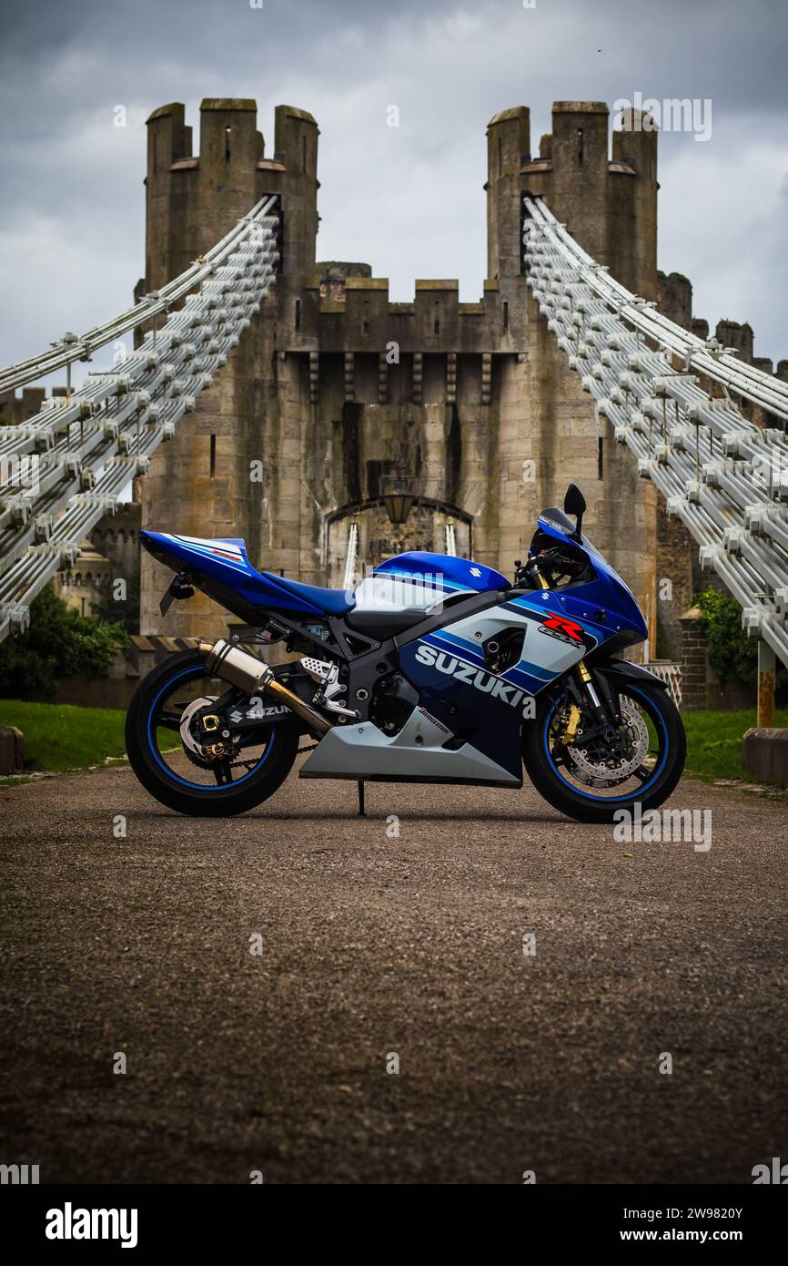 A close-up of a Suzuki motorcycle parked against a backdrop of  walking bridge in Conwy, Wales Stock Photo