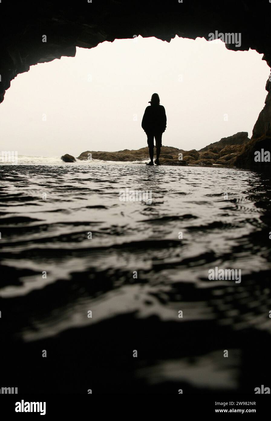 A woman stands in water silhouetted in the mouth of a cave, Oregon. Stock Photo