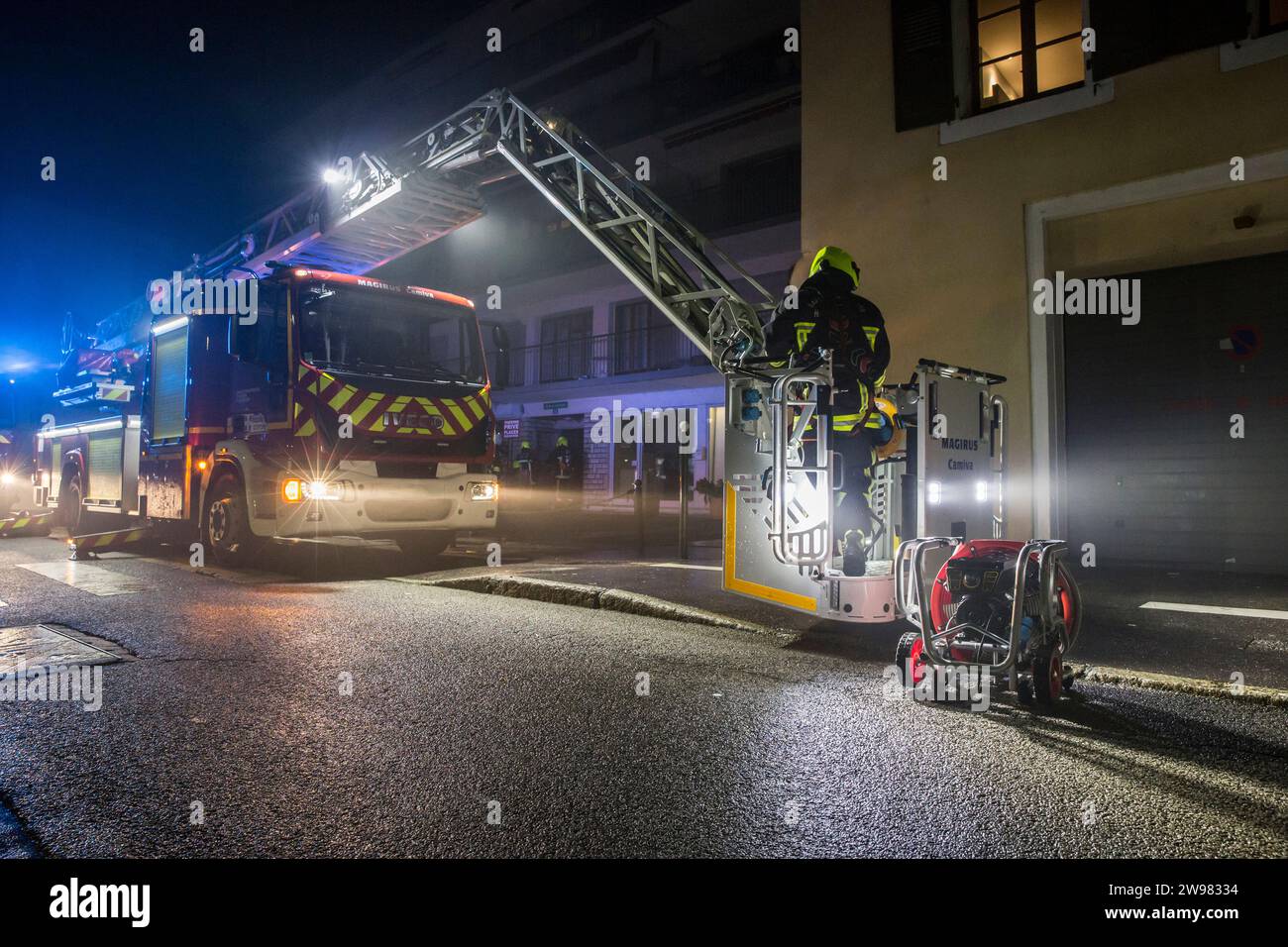 Firefighters loading up big ventilation fan to increase visibility during active fire situation in building at night, Annecy, Haute-Savoie, France Stock Photo