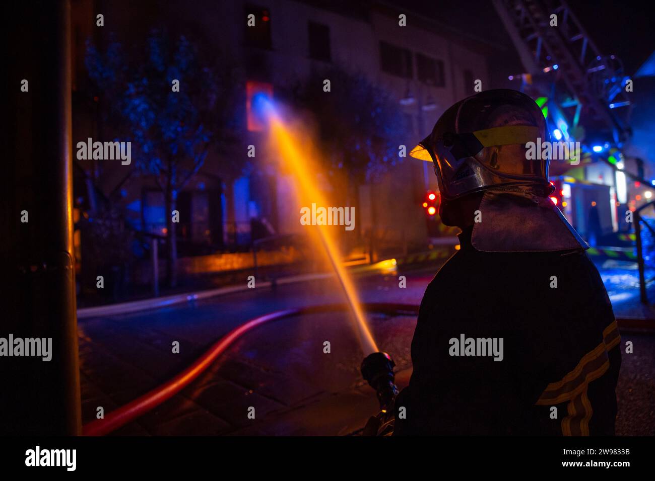 Firefighter spraying water on burning house at night, Haute-Savoie, France Stock Photo