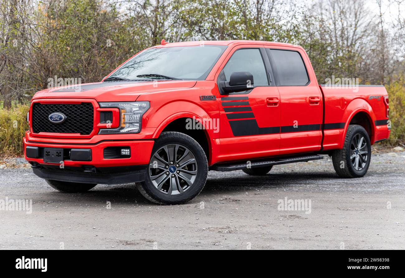 A red Ford F150 Sport pickup truck parked in an outdoor area surrounded by shrubbery and trees Stock Photo