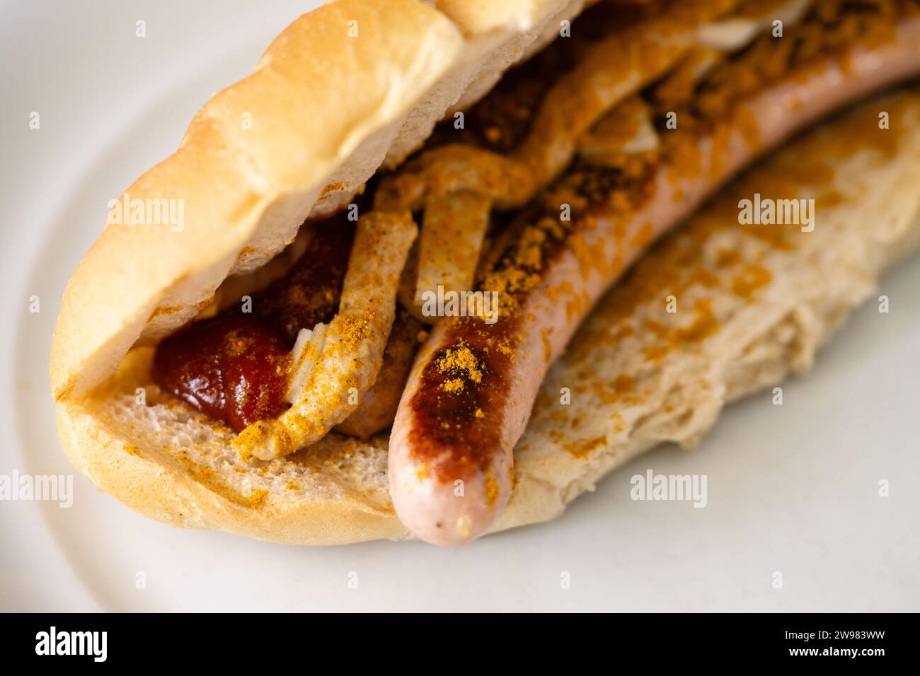 Bosna or Bosner Spicy Austrian Style Hot Dog with grilled Bratwurst, Onions, Tomato Ketchup and Curry in Selective Focus Stock Photo