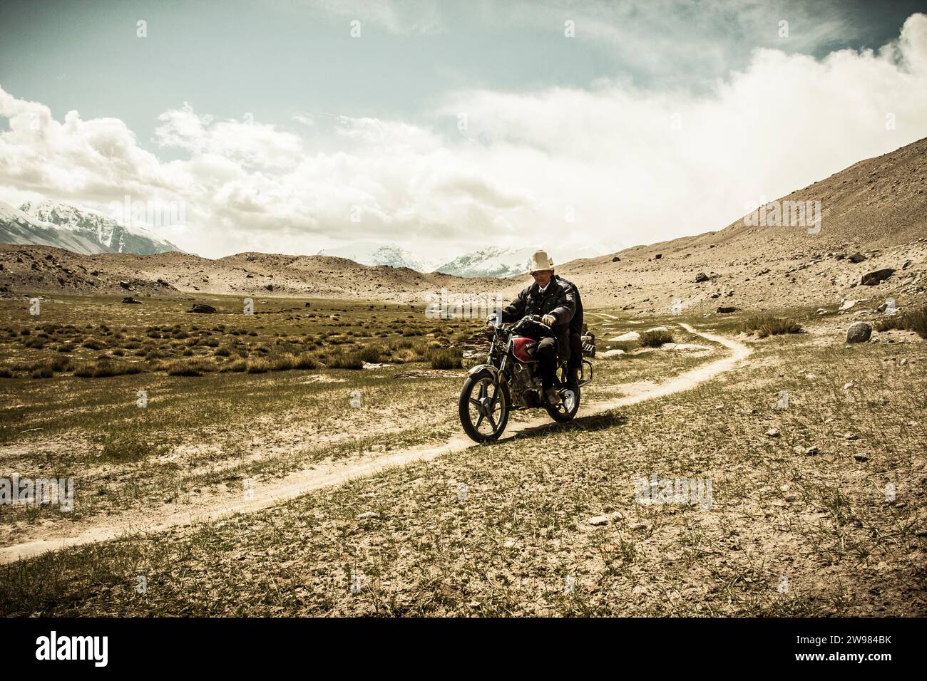 Tajik Man riding a motorcycle through the mountains Stock Photo