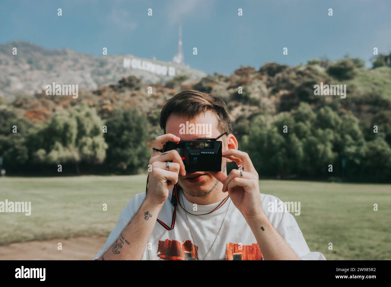 A man with a camera stands on a hilltop, against the Hollywood Sign in Los Angeles, California Stock Photo