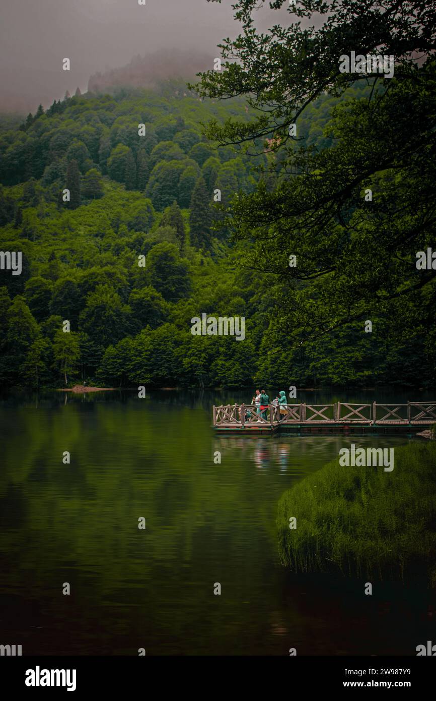 A group of people standing on a rustic wooden bridge, looking out over a tranquil river below Stock Photo