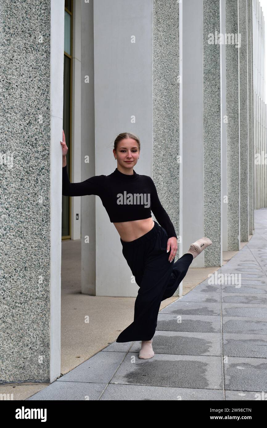 Young woman in black outfit performing a contemporary dance move on a stone sidewalk Stock Photo