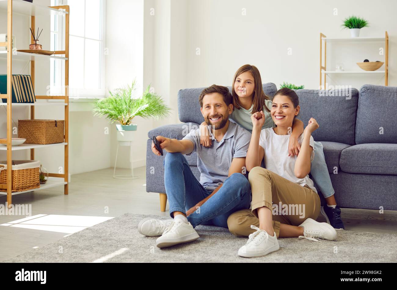 Excited happy young family with child girl watching tv in the living room at home. Stock Photo