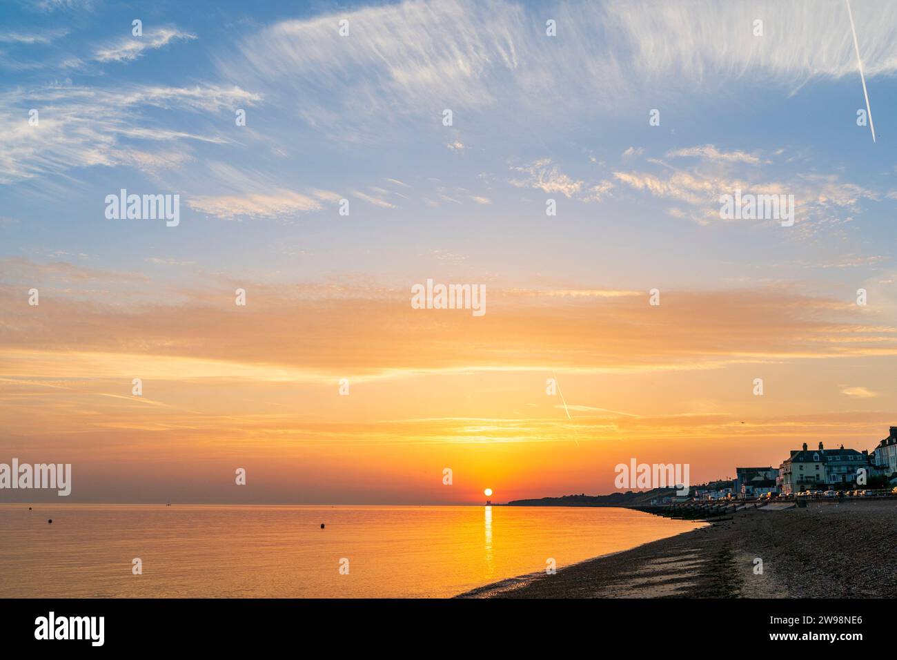 Wide angle shot, sunrise over the beach at Herne Bay with the sun directly over the distant ruins of the 12th century Anglo-Saxon church at Reculver. Stock Photo