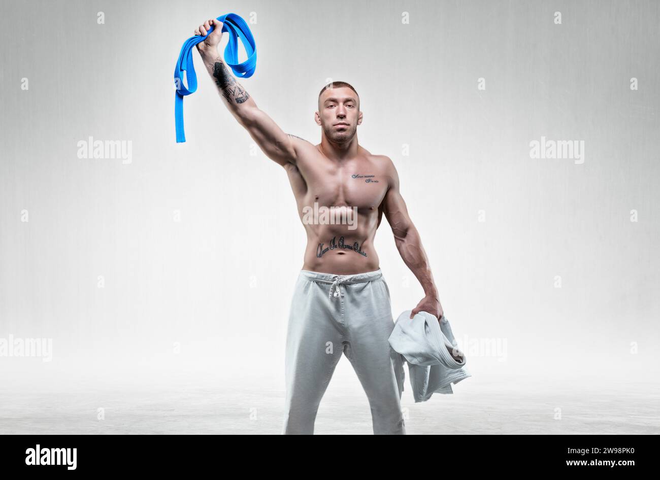 The athlete triumphantly lifts the blue belt up. Concept of karate, sambo, jujitsu. Mixed media Stock Photo