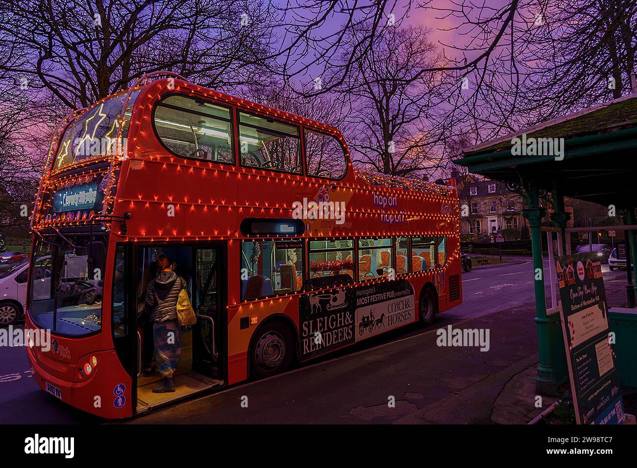 As twilight draws near, a festive double-decker bus festooned with twinkling yellow lights awaits as a passenger boards, Harrogate, Yorkshire, UK. Stock Photo