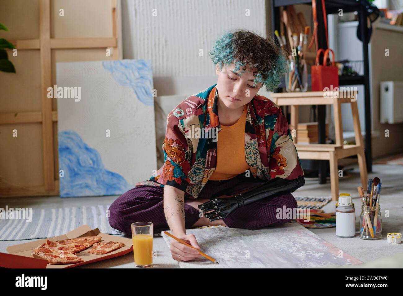 Creative young woman with prosthetic arm having pizza when drawing on canvas Stock Photo