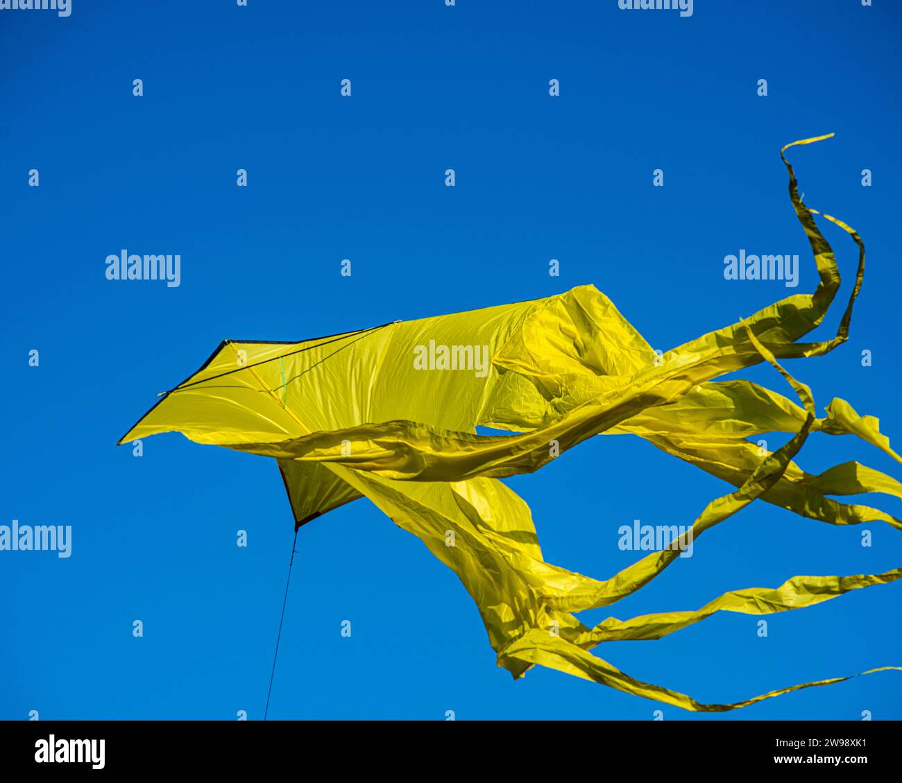A vibrant yellow kite soaring through a bright blue sky. Stock Photo