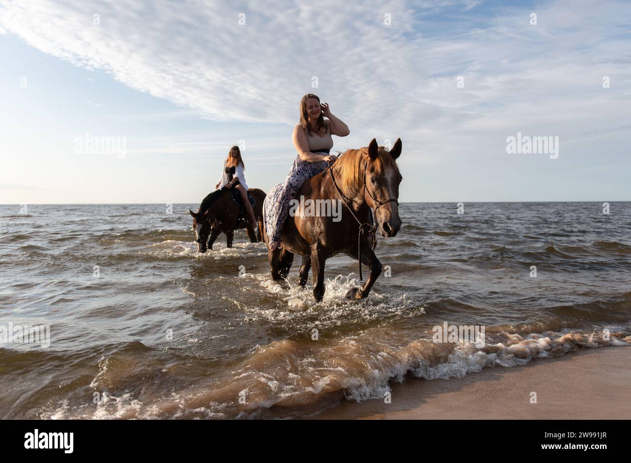 Two female riders galloping on horseback through the shallow waters of a coastal beach Stock Photo