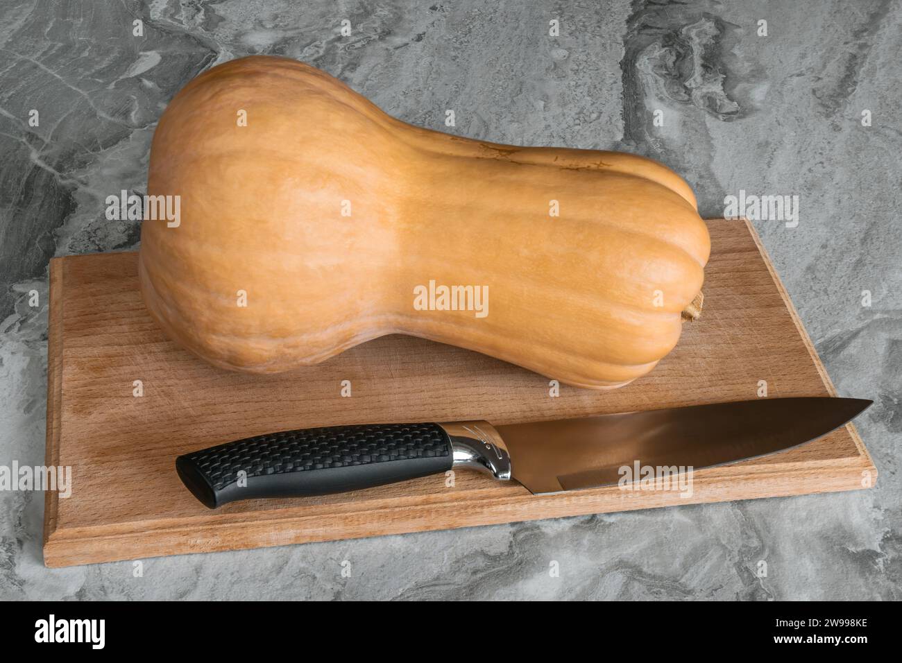 Butternut squash (Cucurbita moschata), known as butternut pumpkin or gramma lying on a cutting board with a knife Stock Photo