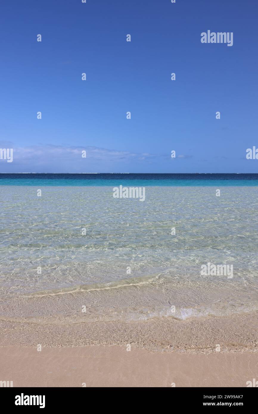 A pristine beach with crystal-clear waters, inviting white sand, and a bright blue sky Stock Photo
