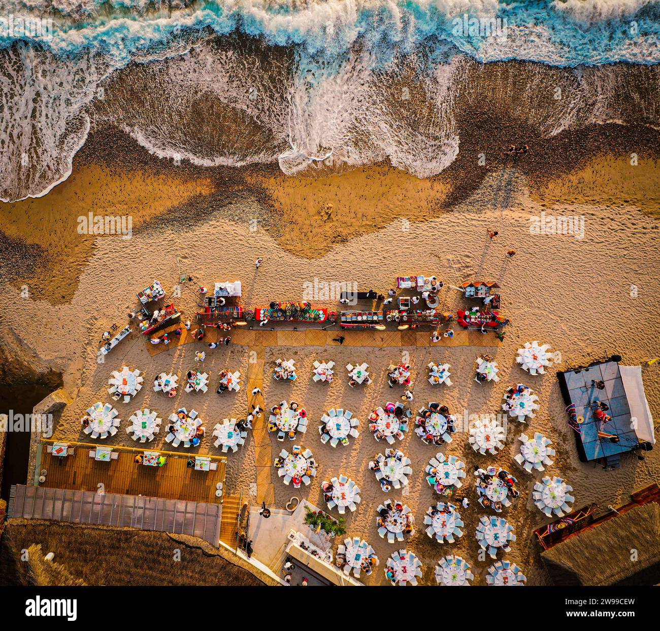 Top down shot of a mexican beach at the sunset with sand and water. Mexican party with tables and people. Stock Photo