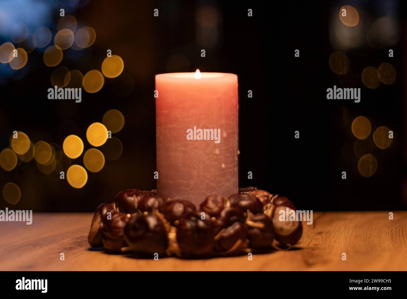 Christmas candle with ring of chestnuts on brown tabel and christmas tree in background bokeh with blurred lights Stock Photo