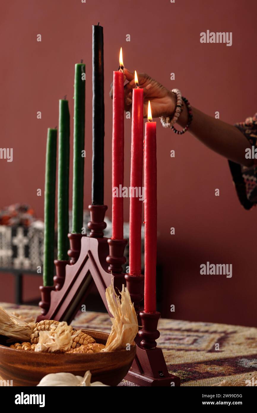 Hand of young unrecognizable African American woman igniting candles on candleholder while preparing for celebration of Kwanzaa Stock Photo