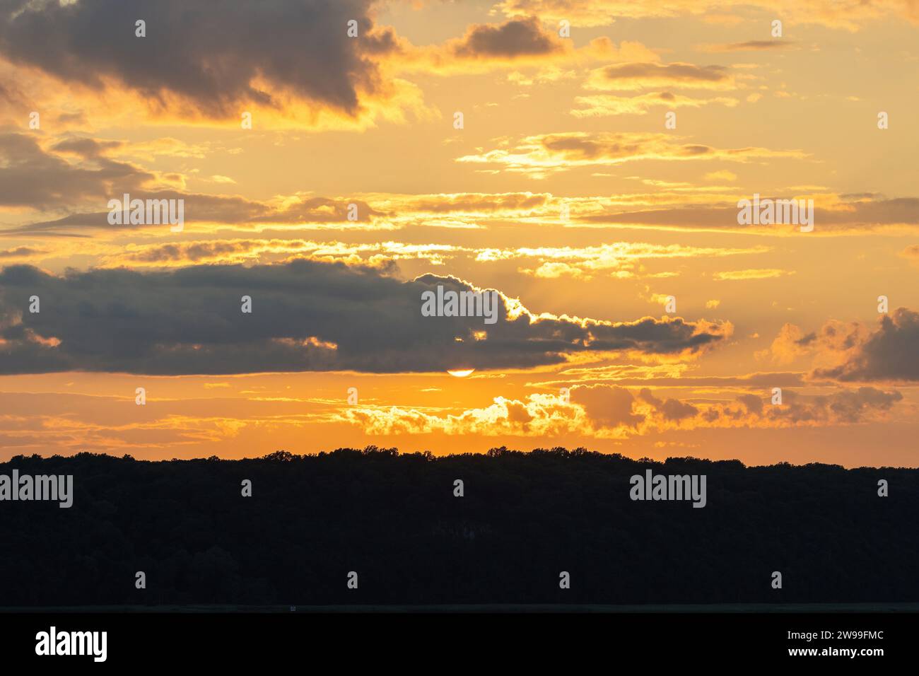A serene landscape with vibrant yellow sunset skies partially obscured by clouds, featuring a horizon line composed of both land and water Stock Photo