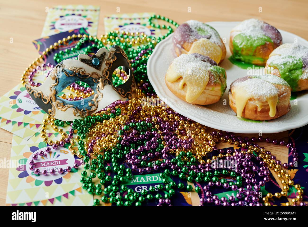 Group of Mardi Gras symbols such as postcards, venetian mask, colorful beads and appetizing homemade berliner donuts on table Stock Photo