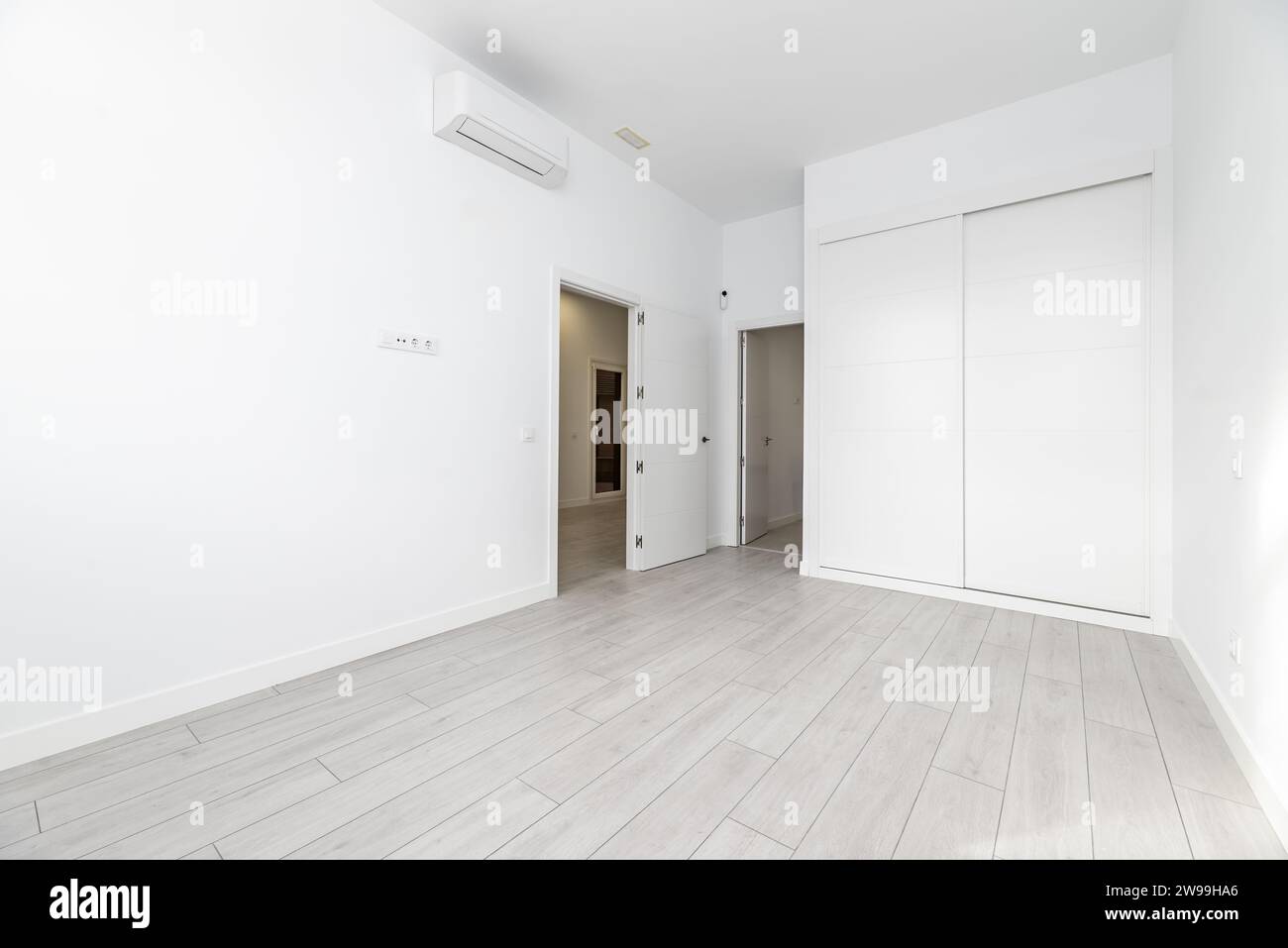 An empty room with built-in wardrobes with white sliding doors, access to an en-suite bathroom and air conditioning units hanging high on the wall Stock Photo