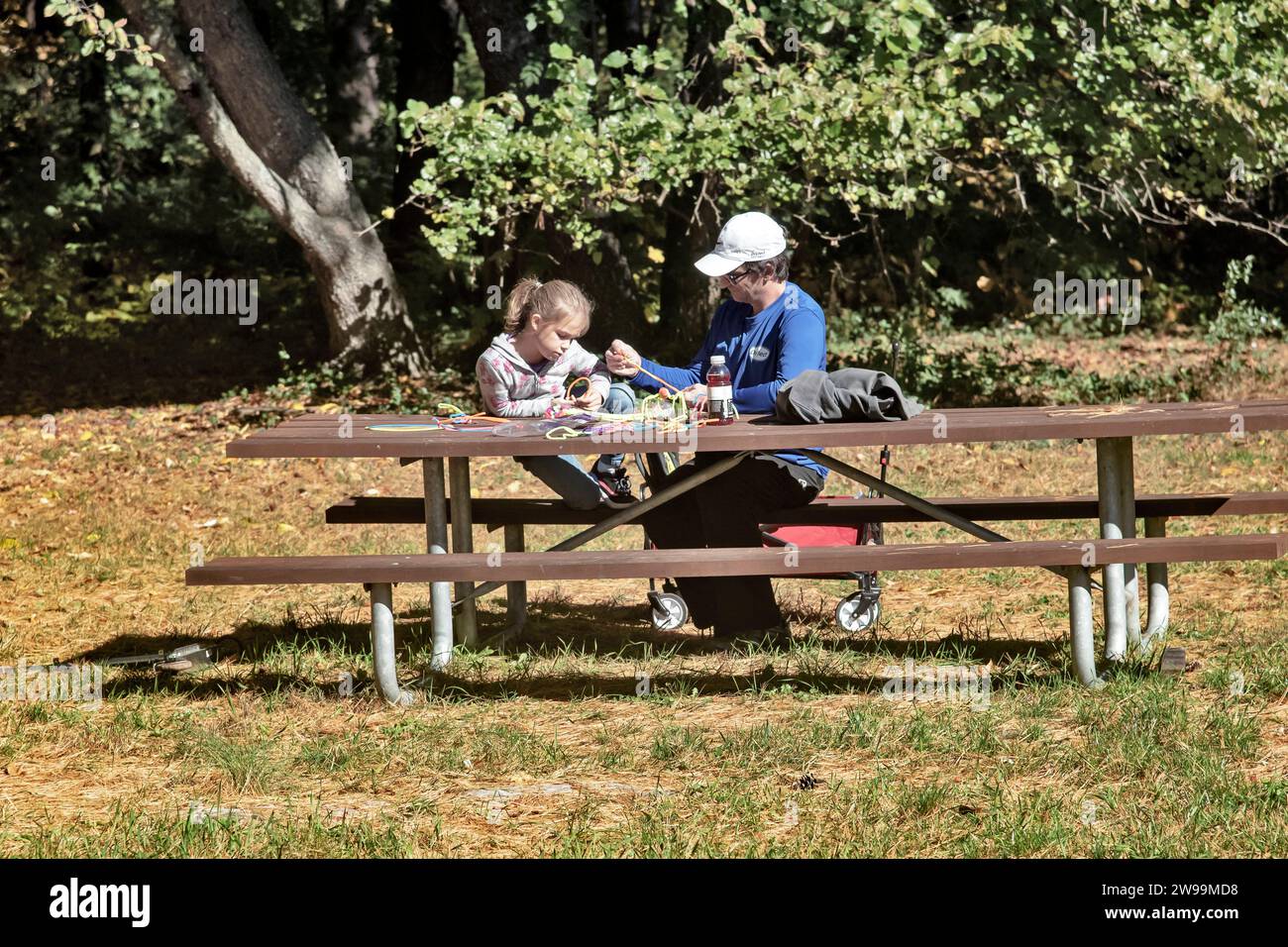 A 6-8 year old girl with her dad in the park making something at a wooden table, Neshaminy Park, Philadelphia, USA Stock Photo