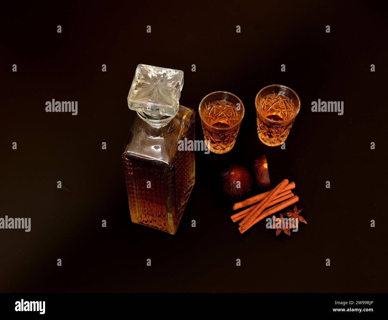 Fig liqueur, strong homemade alcohol with cinnamon, anise in two glasses and a crystal decanter on a black background, next to ripe fruits. Close-up. Stock Photo
