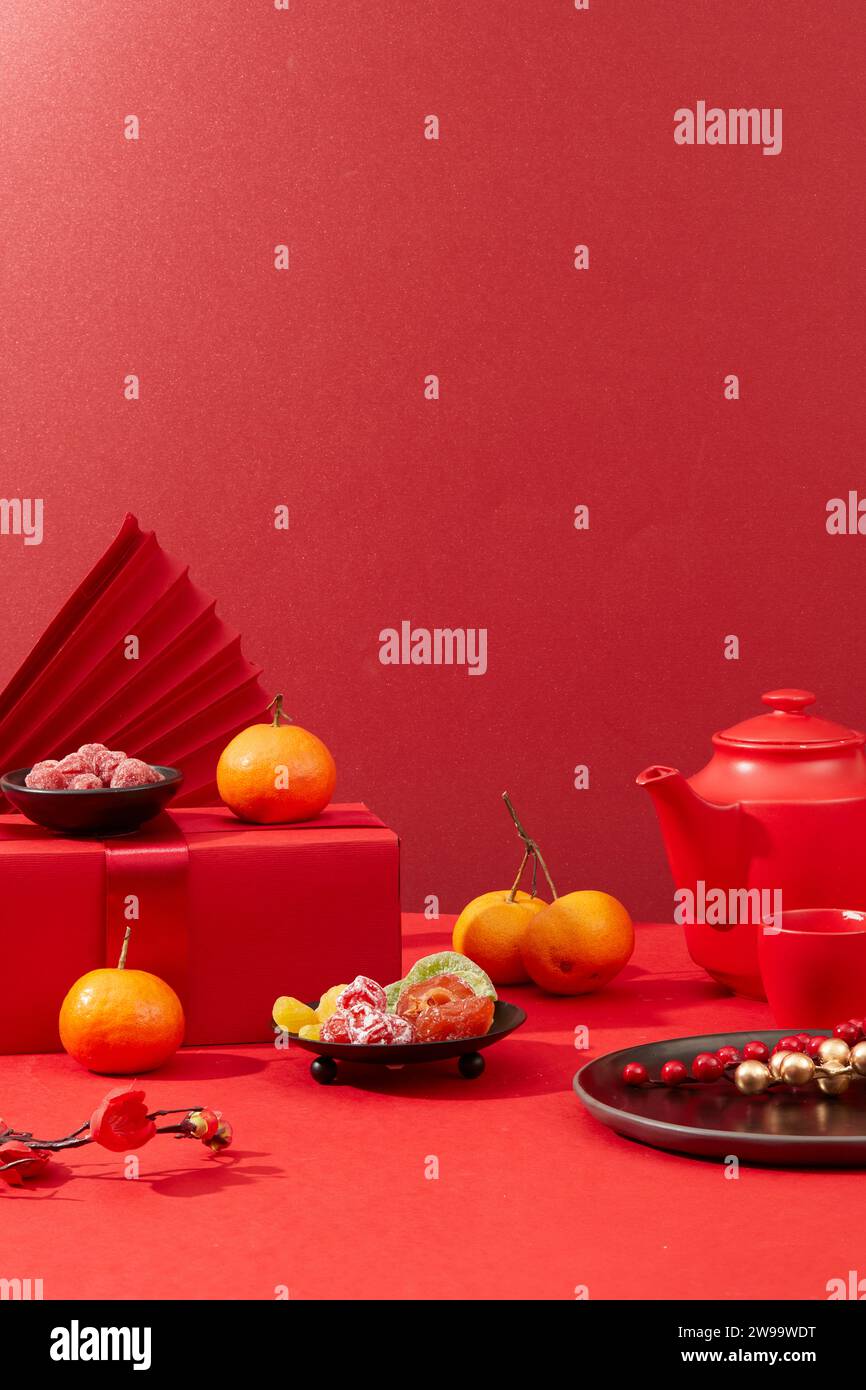 A tea set, jam, salted dried fruit, tangerines, red gift boxes and paper fans are arranged on a background filled with red. Tet decoration with front Stock Photo