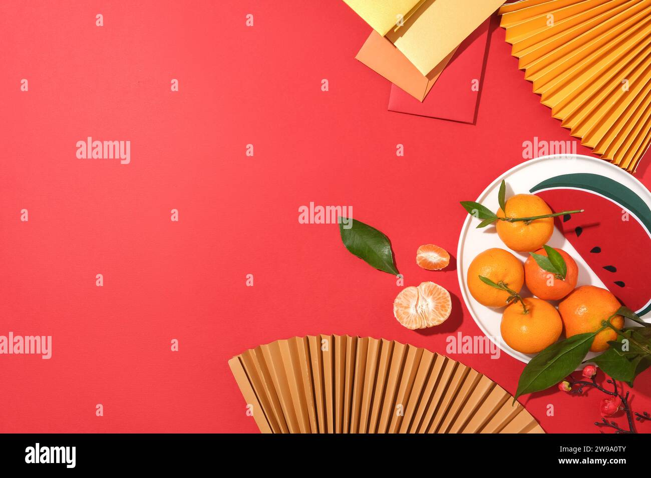 On a bright red background, paper fans, fruit dish and lucky money envelopes are decorated on the right side of the frame. Space on the left for text Stock Photo