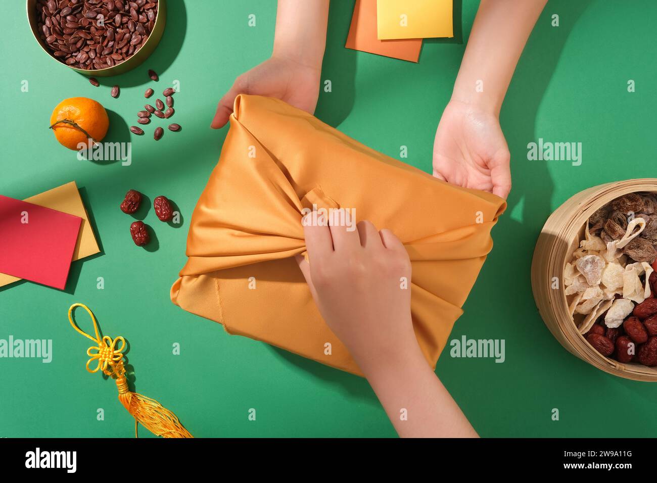 Tet gift giving scene. Gift box in the center of the frame, melon seed tray, jam tray and lucky money envelope on green background with top view. Stock Photo