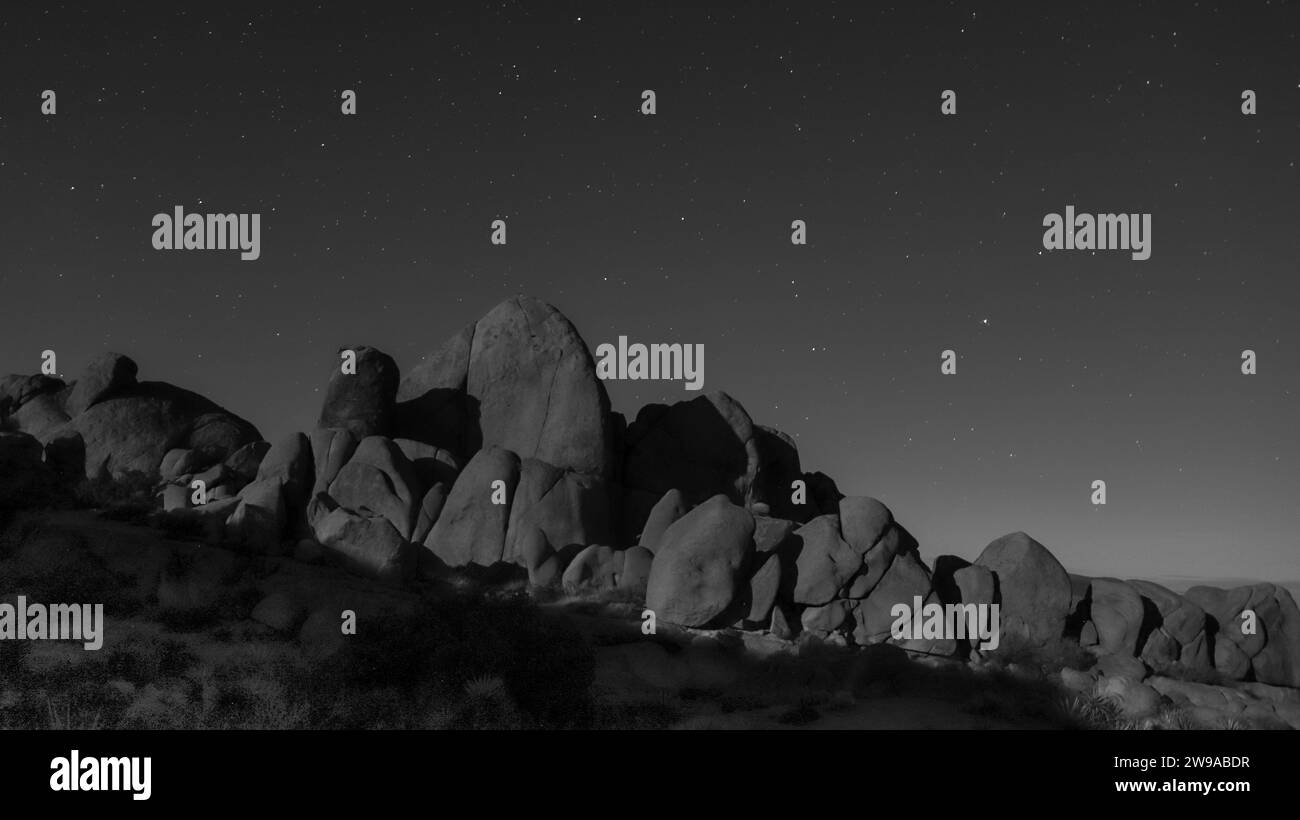 A stunning black and white of a starry night sky over a rocky landscape Stock Photo