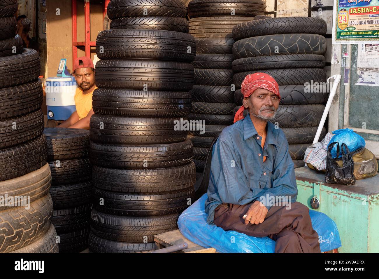 Two Indian men sitting next to piles of old and new tyres in a semi-open air tyre and tyre repair shop in Grant Road, Mumbai, India Stock Photo