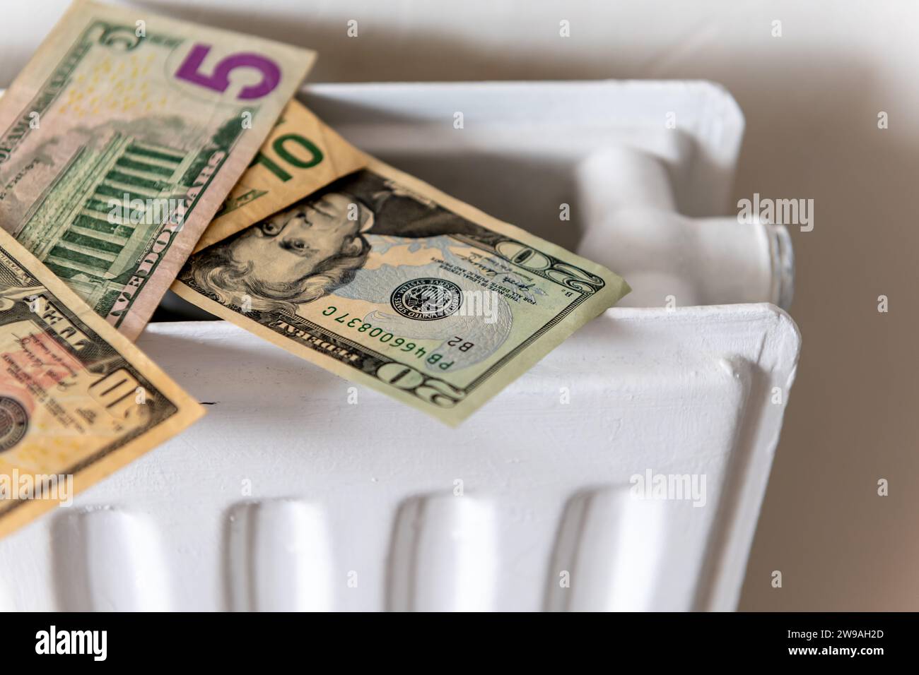 A bunch of US Dollars on top of a central heating radiator. A heating, energy cost concept. Stock Photo