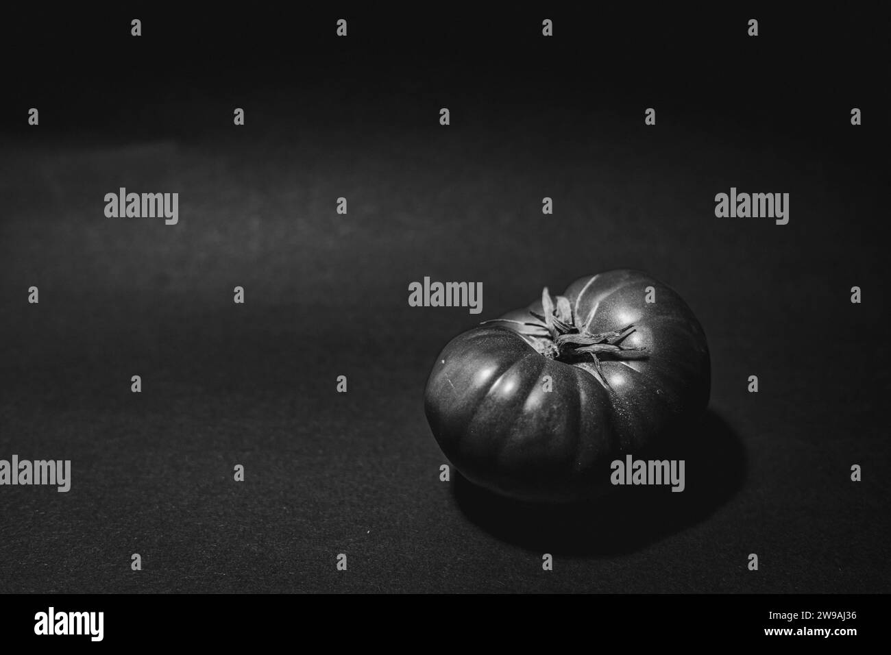 A grayscale shot of a ripe Spanish tomato on a solid tabletop, isolated on a blank background Stock Photo