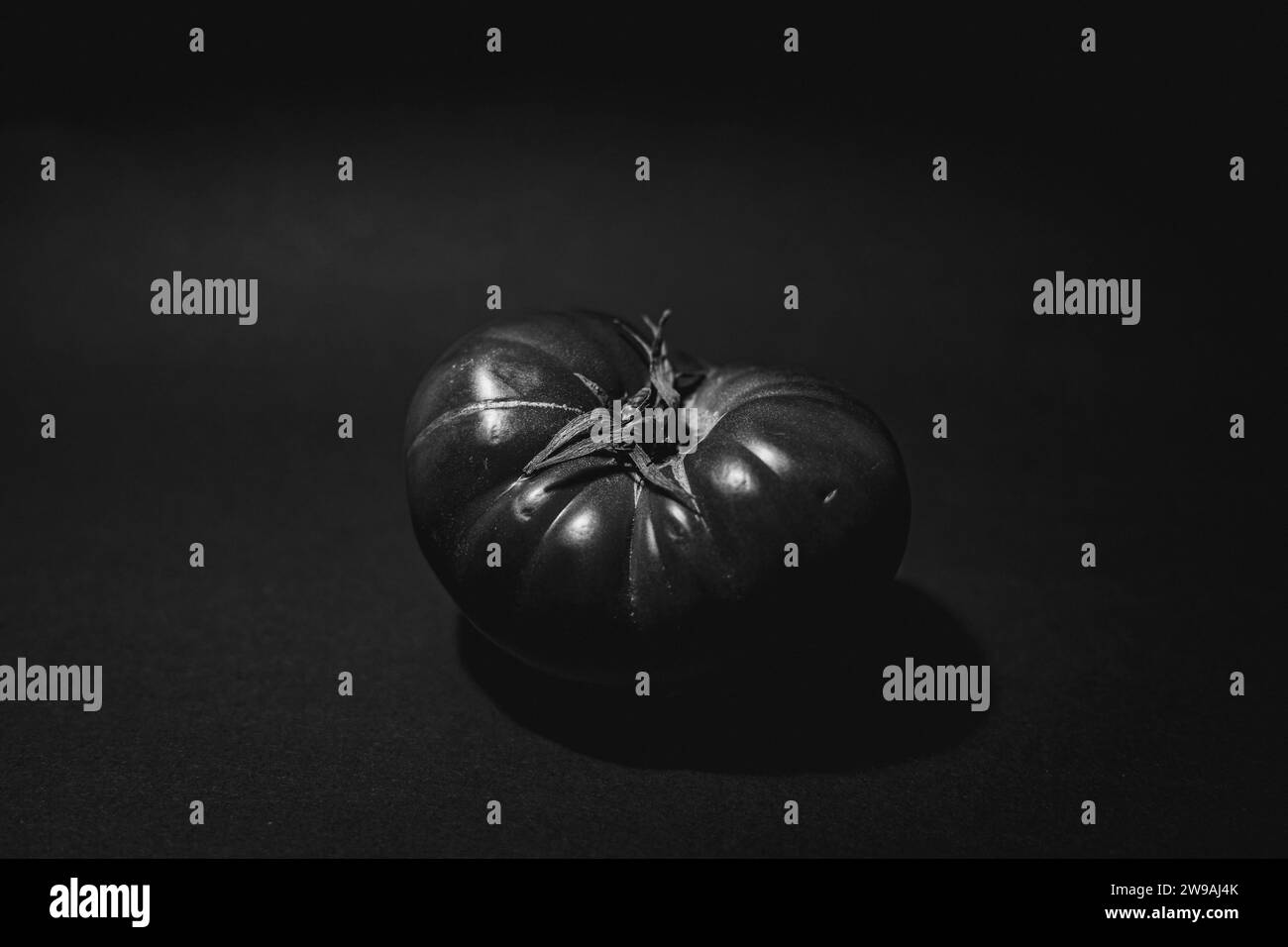 A grayscale shot of a ripe Spanish tomato on a solid tabletop, isolated on a blank background Stock Photo