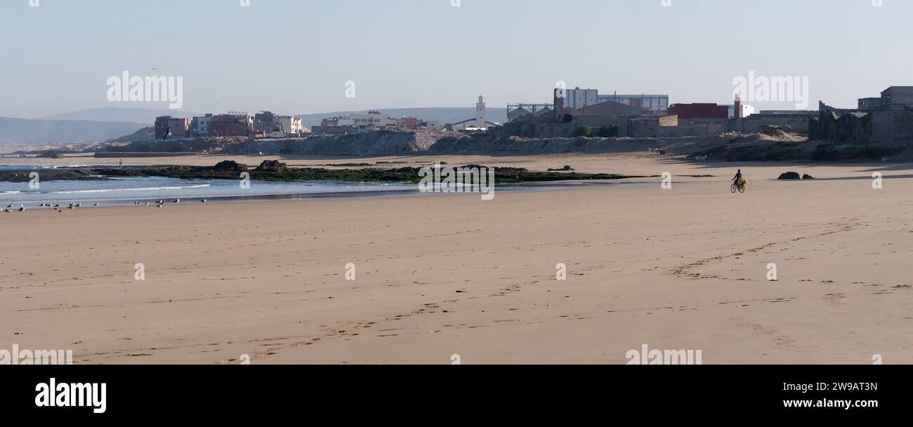 Vast sandy beach and rubbish piles on the industrial side of Essaouira with a lone cyclist, Morocco. December 26, 2023 Stock Photo