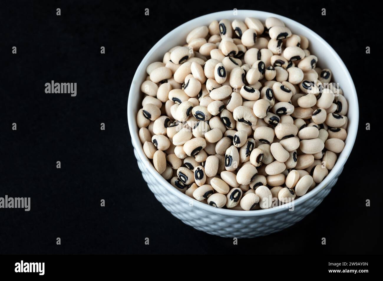 Black eye peas in a white bowl on black background, top view. Black