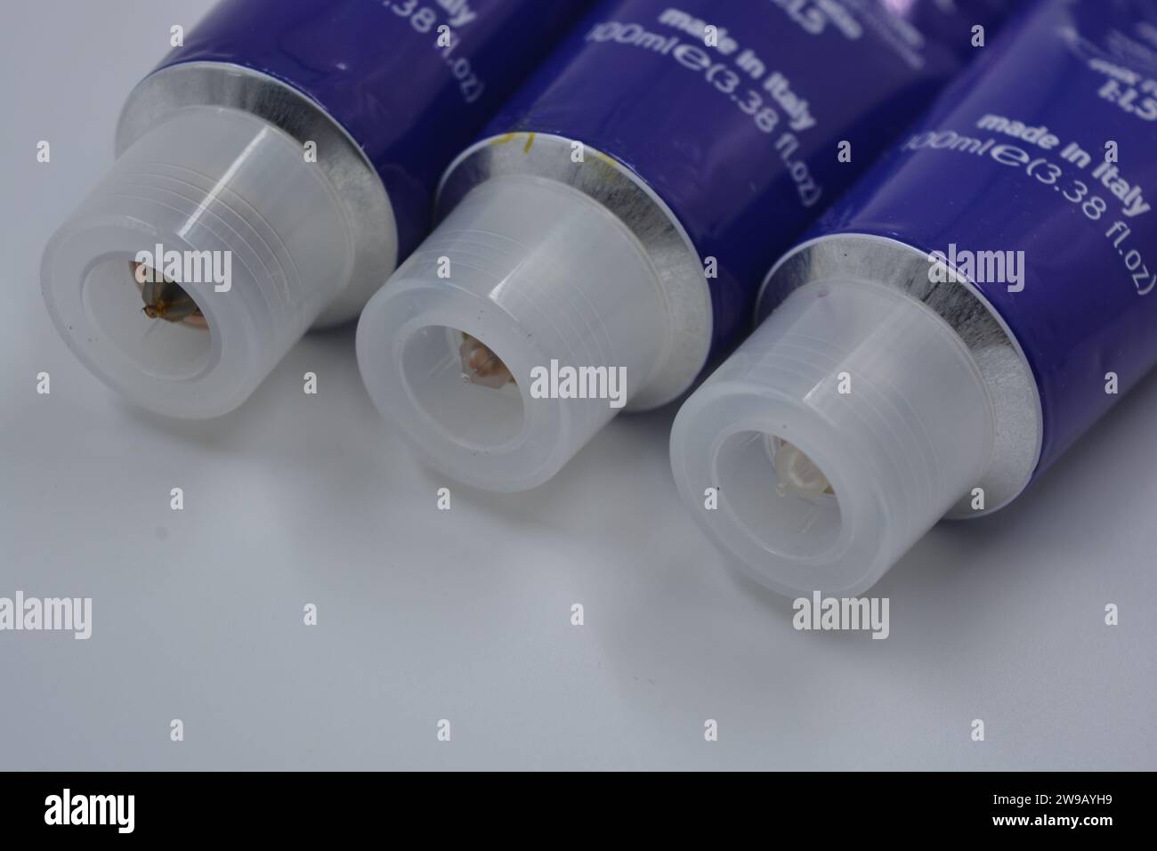 Three metal tubes of women's hair dye with large, clear, plastic lids are arranged on a white, matte background. Stock Photo