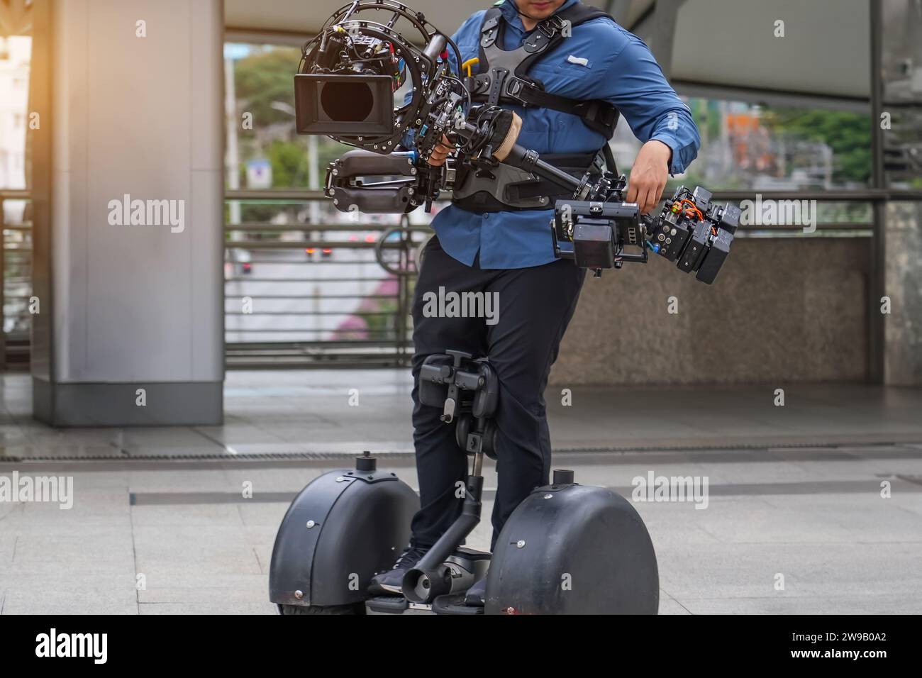 Videography, filmmaking and creativity concept - close up of modern movie camera on 3-axis gimbal stabilizer in male hands go rides a segway. Stock Photo