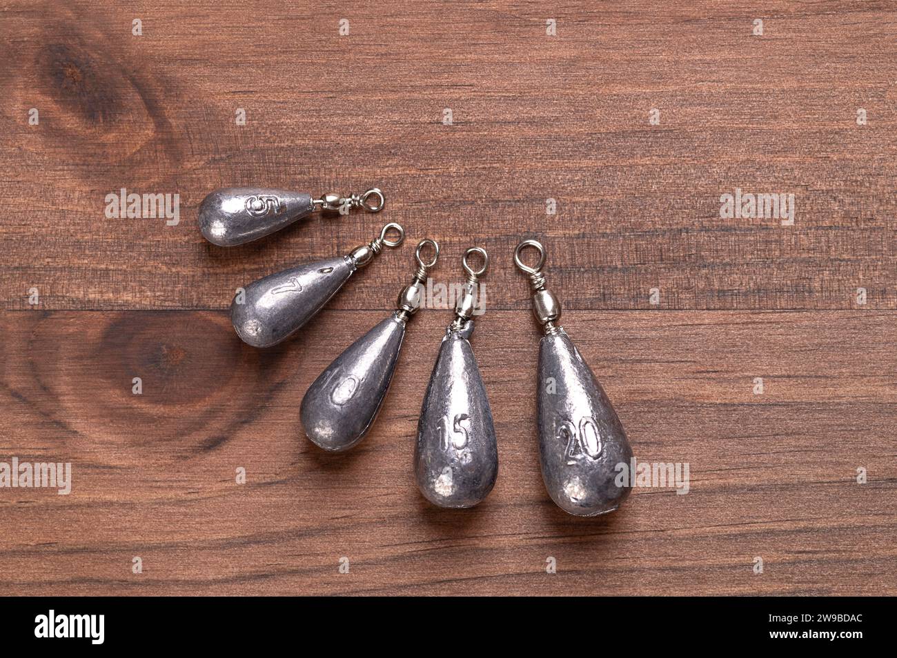 Fishing pear leads, also called sinkers, on a dark brown wood board, from above. Six different pear-shaped lead weights for fishing. Stock Photo