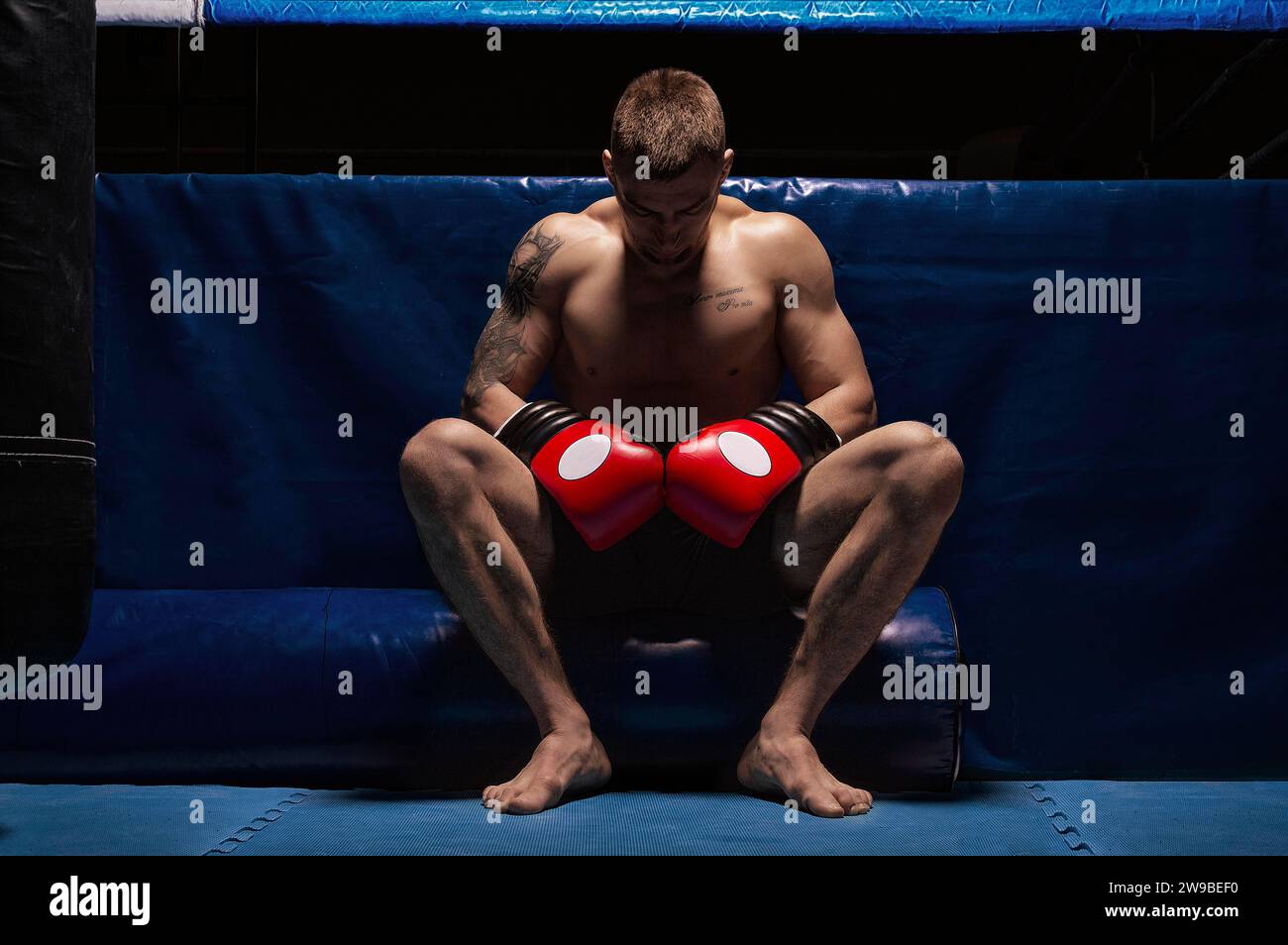 Boxer sits in gloves near the ring with his head bowed. The concept of sports, boxing, mixed martial arts, sports betting. Mixed media Stock Photo