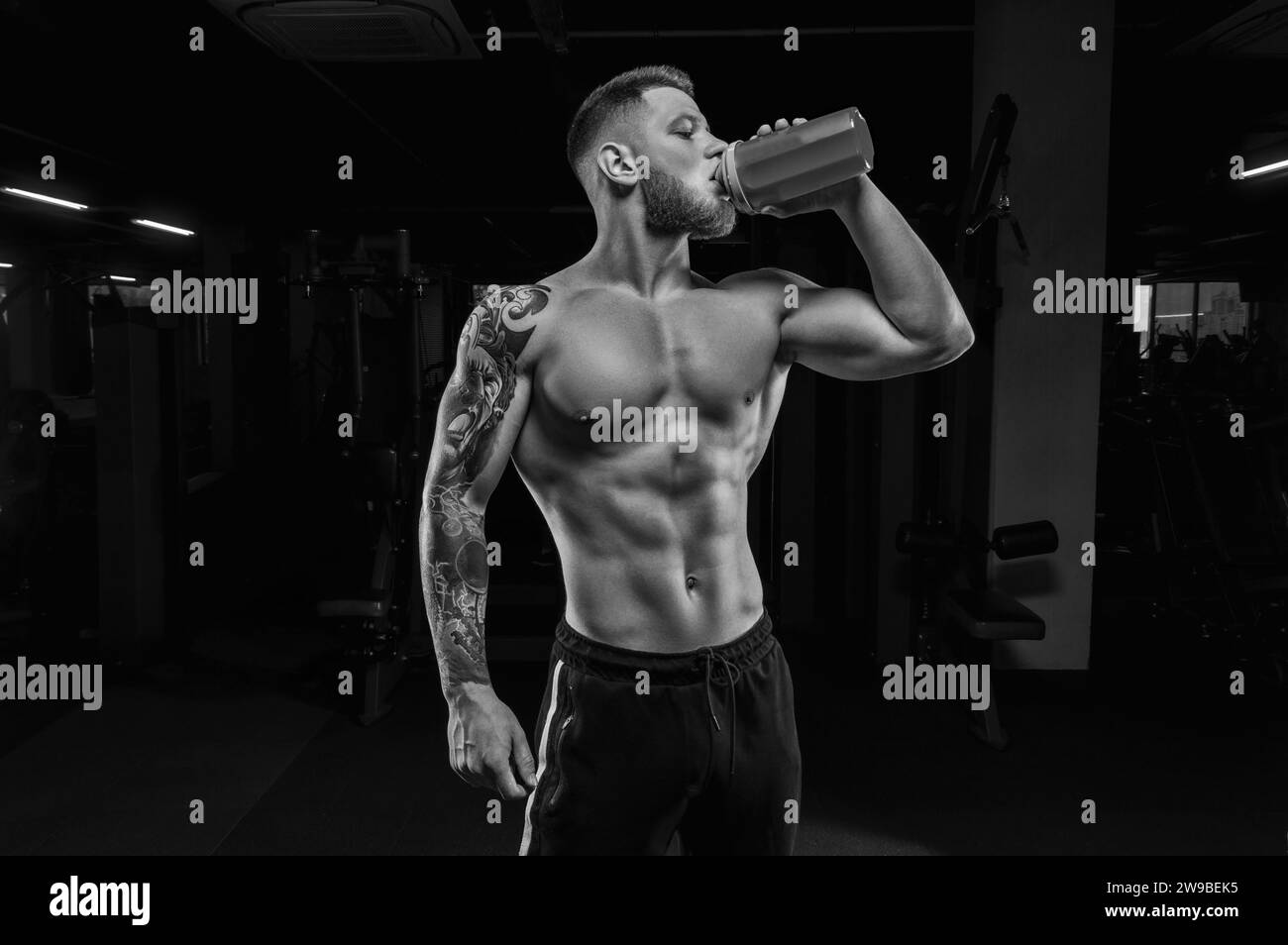 Portrait of an athlete drinking from a shaker in the gym. Bodybuilding and fitness concept. Mixed media Stock Photo