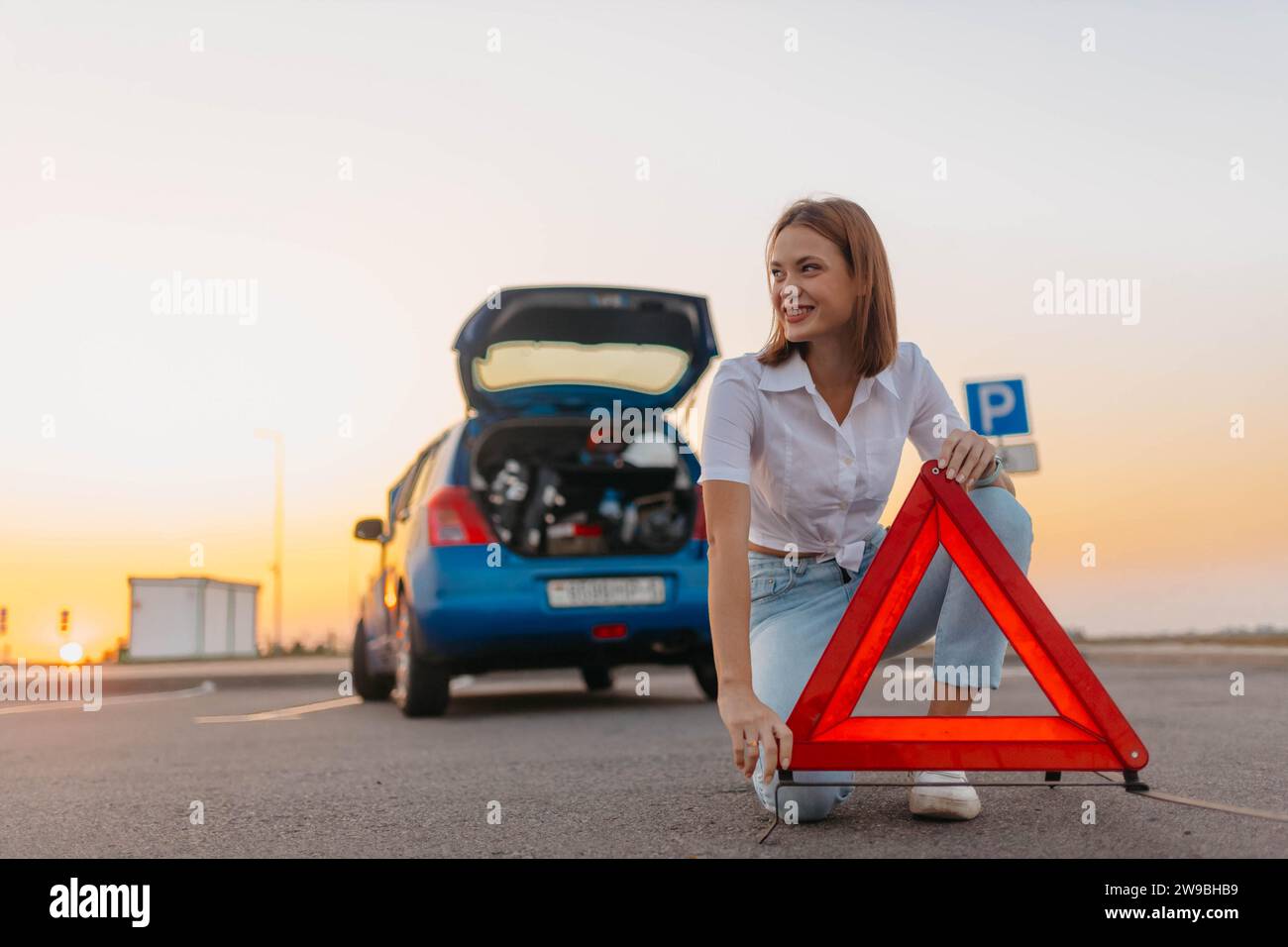 Young beautiful and hot woman driver installs a warning triangle, safety rules while traveling, car breakdown Stock Photo