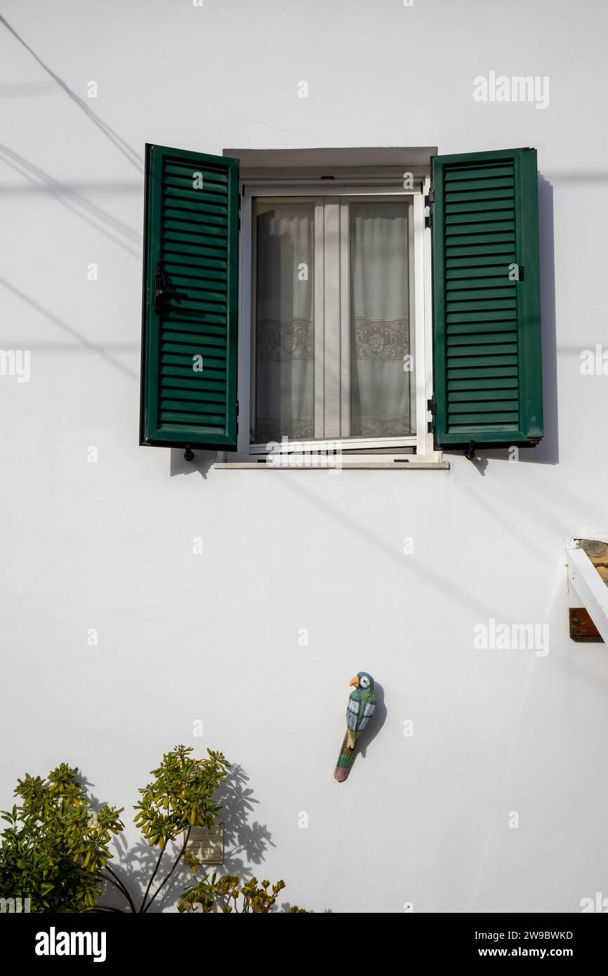 Detail of the White house, where was living british writer Lawrence Durrell. Window with green opened shutters. Wooden parrot decorating the wall. Kal Stock Photo