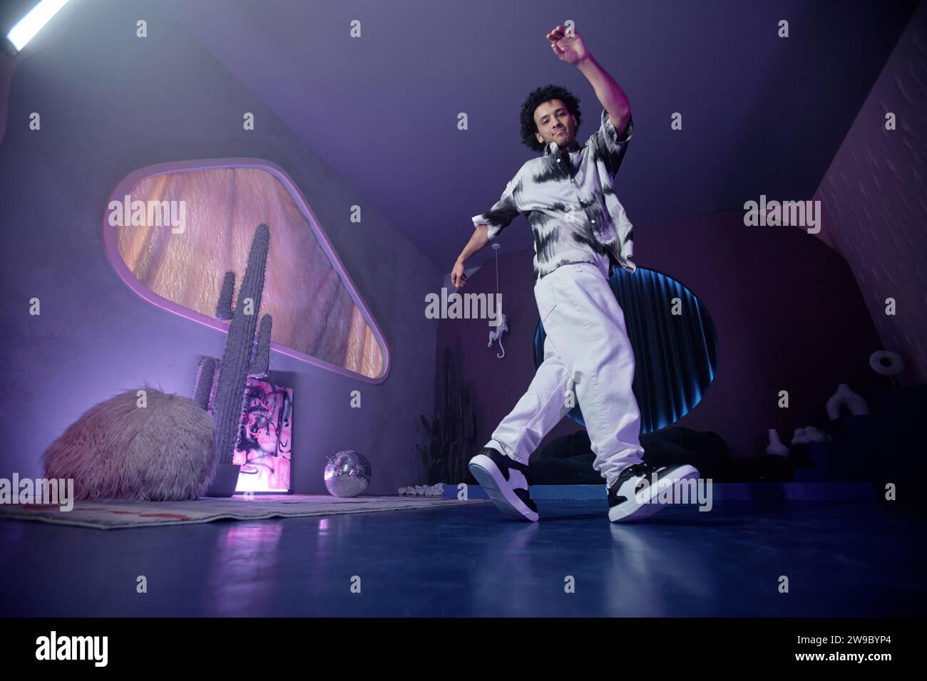 Young male hip-hop dancer demonstrating moves in contemporary art space with dim light Stock Photo
